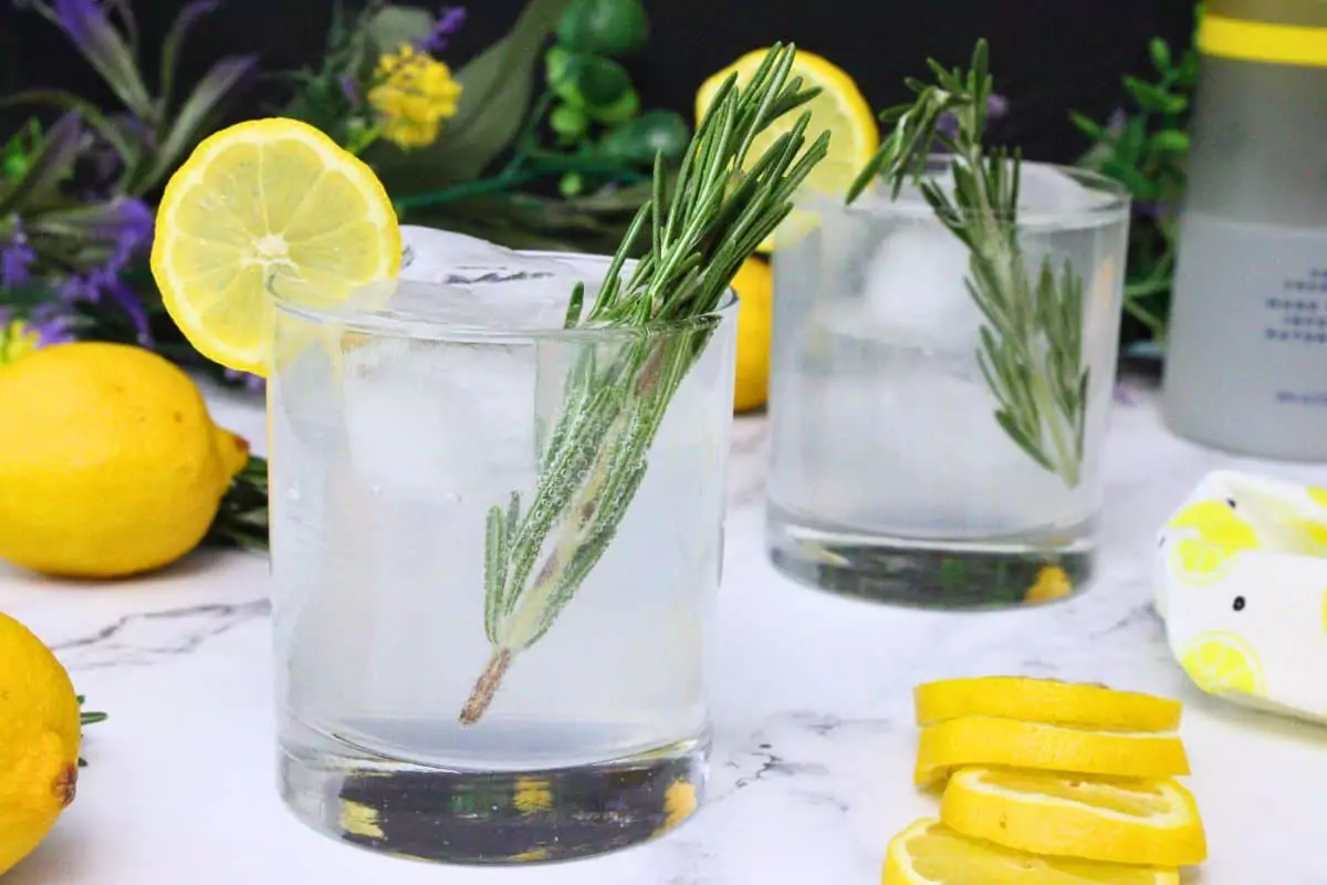 sparkling lemonade cocktail in the foreground with another in the back surrounded by lemons and flowers