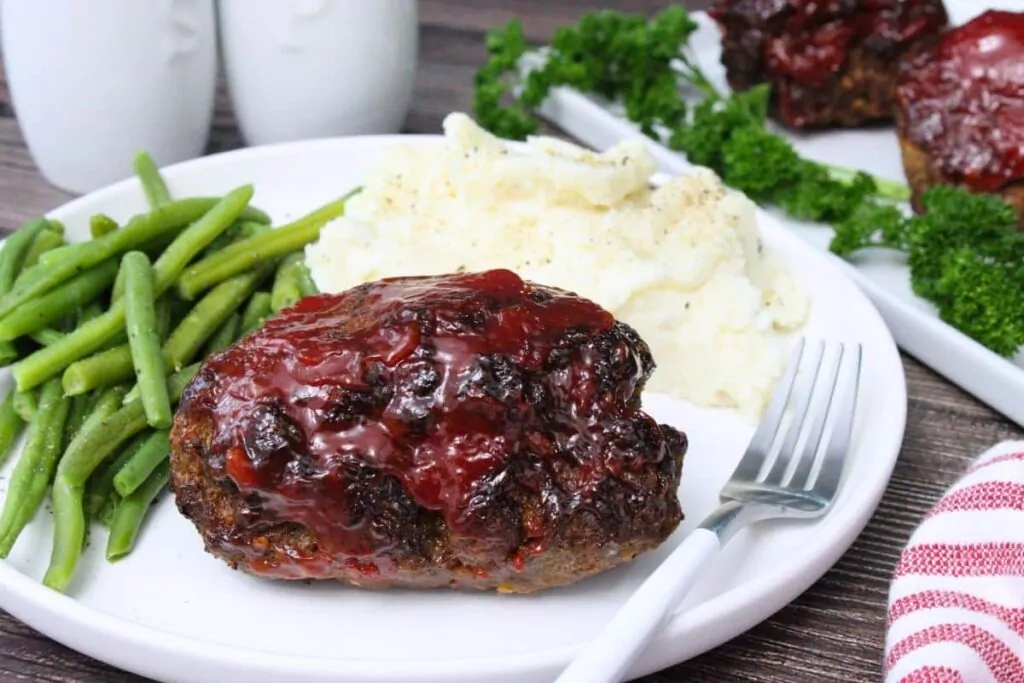 uncut mini meatloaf with hot honey glaze on a plate with green beans, mashed potatoes, and a fork