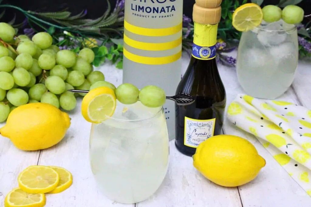 vodka lemonade spritzer with fruit garnish next to vodka and prosecco bottle surrounded by fresh spring decor