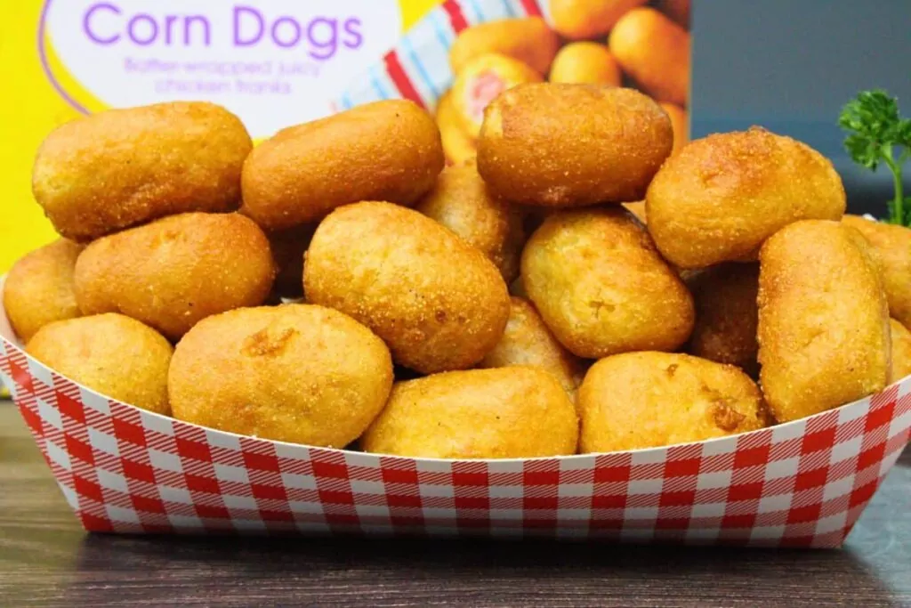 checkered basket filled with golden brown air fryer mini corn dogs in front of the box