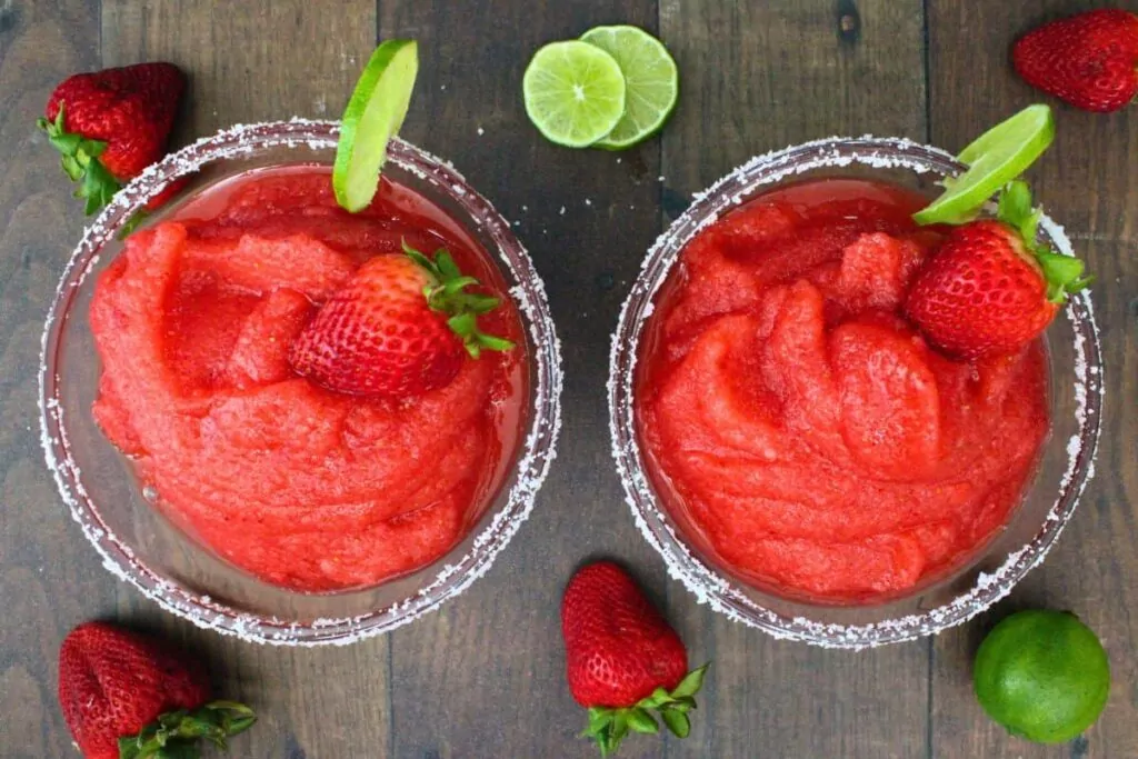 overhead view of two frozen strawberry margaritas with salt rim, strawberry, and lime