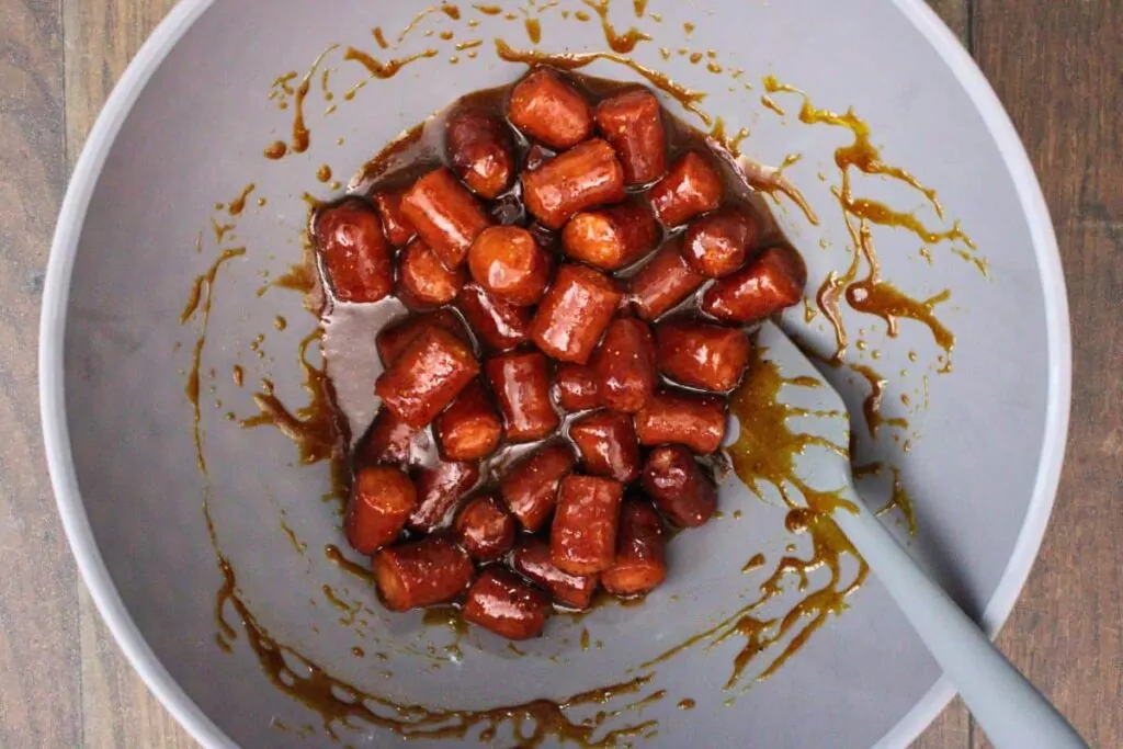 toss hot dog pieces in a bowl with bbq glaze ingredients