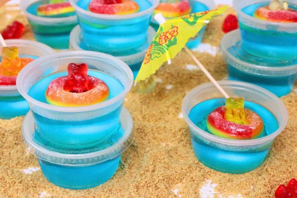pool party jello shots with gummy bears and peach rings on a sandy beach made of graham cracker crumbs