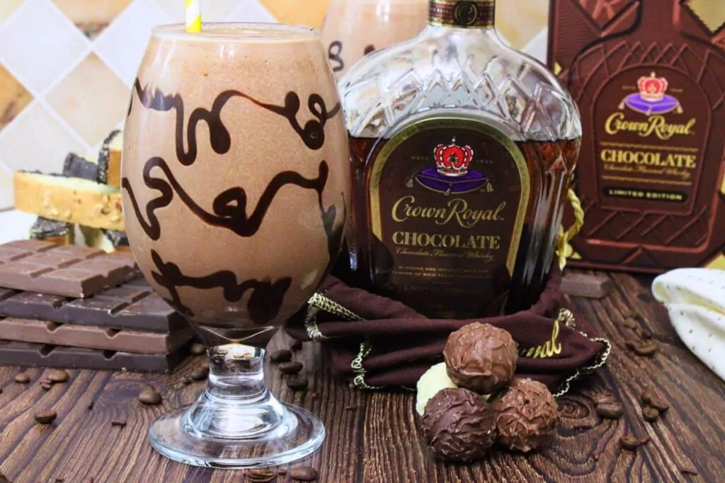 chocolate mudslide with chocolate drizzle in the glass next to chocolate crown royal bottle and chocolate candies