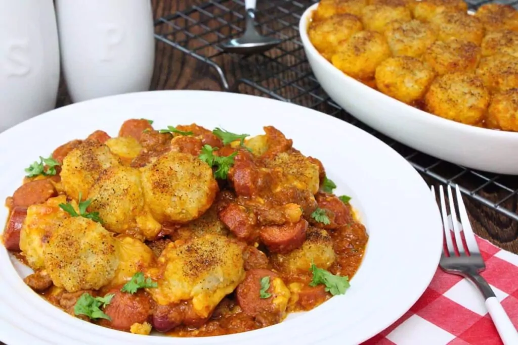 plate with chili cheese hot dog casserole showing off crispy tater tots on top next to warm serving dish
