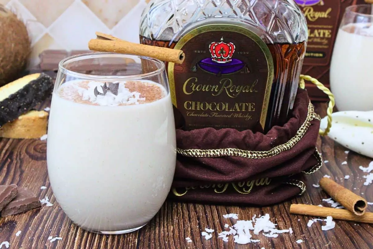 chocolate coquito garnished with cinnamon stick and chocolate curls next to chocolate crown royal bottle