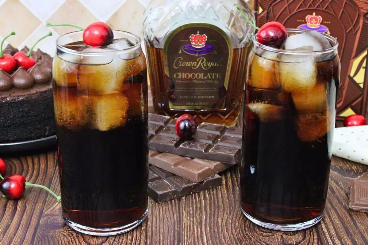 two crown royal chocolate and cherry coke drinks garnished with cherry in front of crown bottle