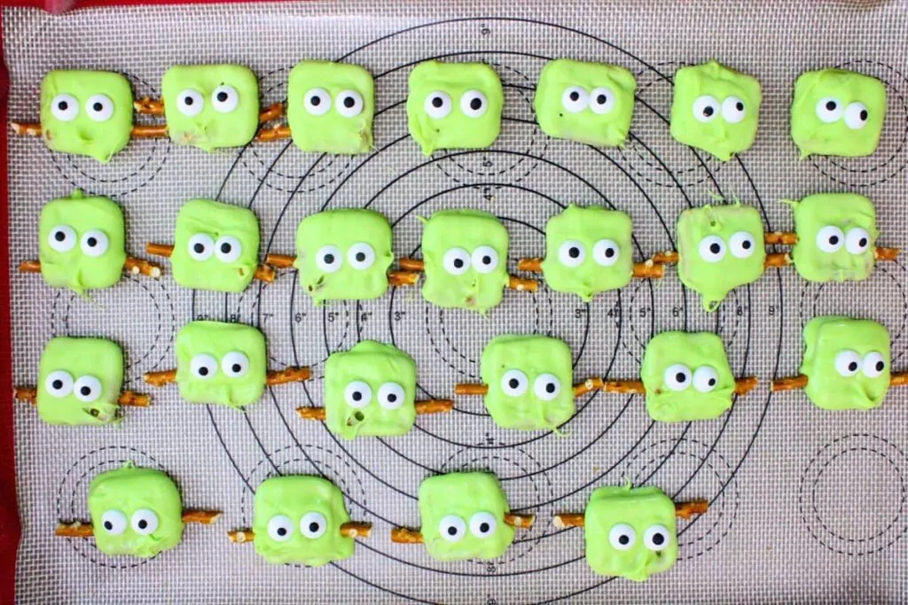 add candy eyes and pretzel rod pieces to chocolate pretzels