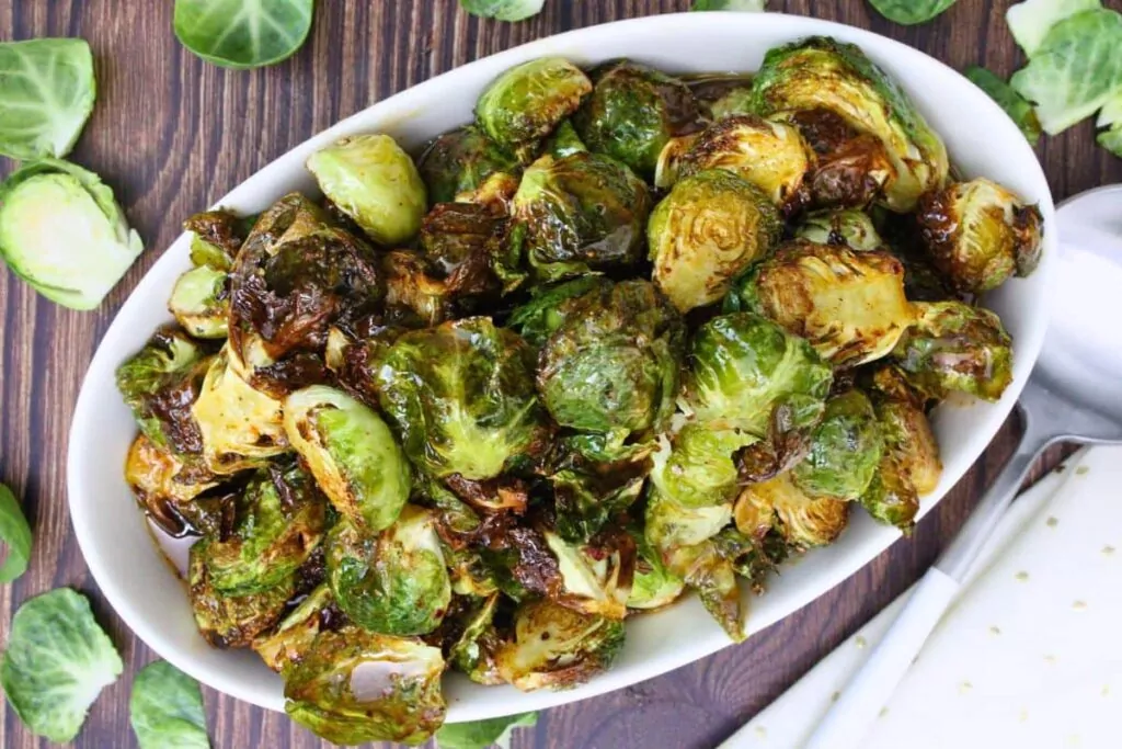 overhead view of copycat longhorn brussel sprouts in an oval serving bowl on a wooden counter