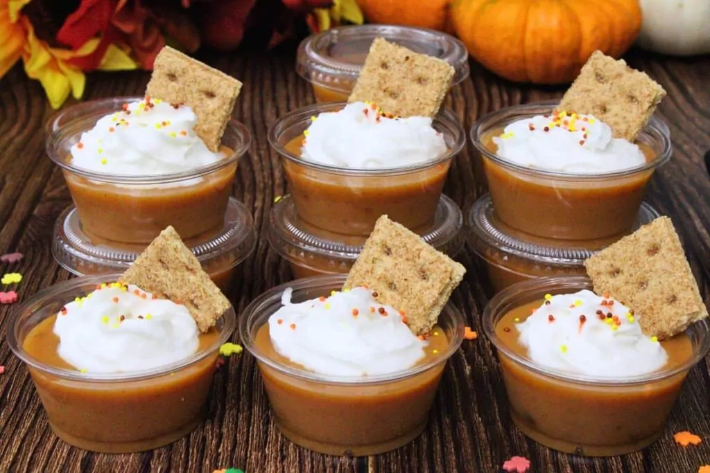 six pumpkin pie pudding shots in two rows topped with whipped cream sprinkles and graham cracker