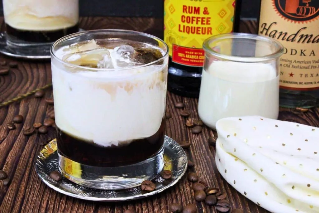 white russian cocktail on a silver coaster in front of cream and liquor bottles