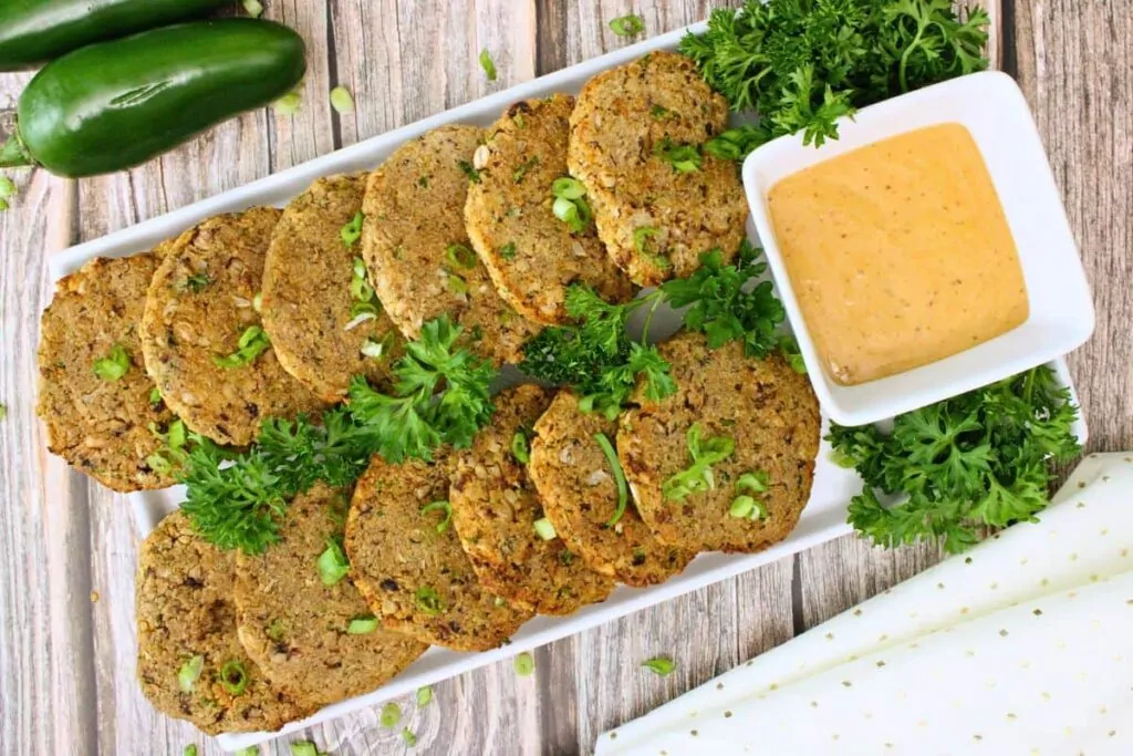 overhead view of black eyed pea fritters lined in rows on a serving platter garnished with parsley, green onions, and remoulade