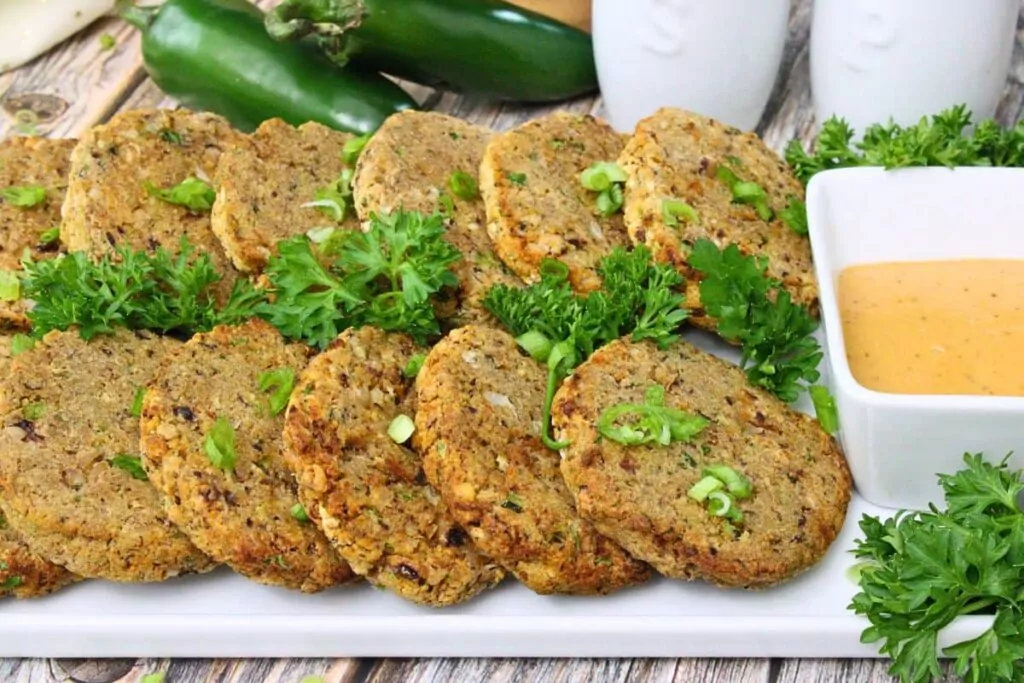 two rows of black eyed pea fritters lined on a serving platter with parsley and green onion garnish and remoulade to the side