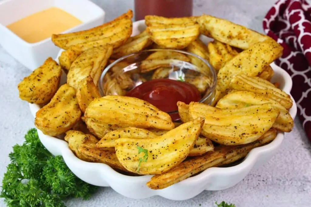 large plate of air fryer potato wedges with a small bowl of ketchup in the center