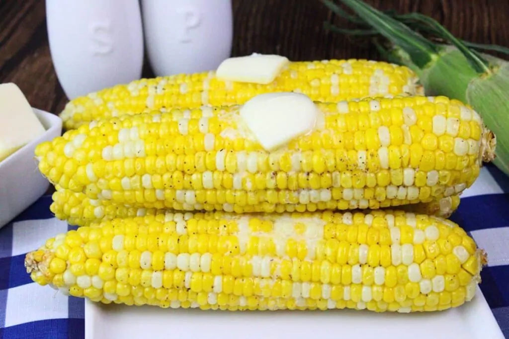 air fryer corn on the cob stacked on a plate and topped with melting butter pads