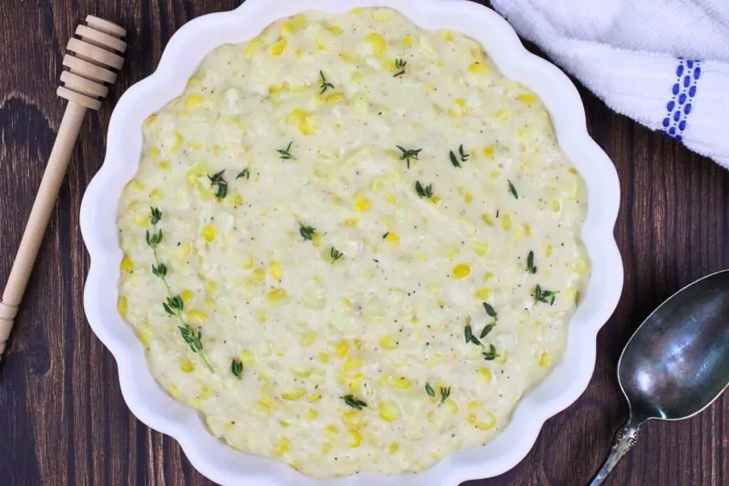 overhead view of creamed corn in a scalloped bowl garnished with thyme