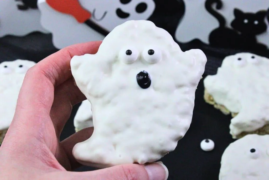 holding up a ghost rice krispie treat with candy eyes and icing mouth